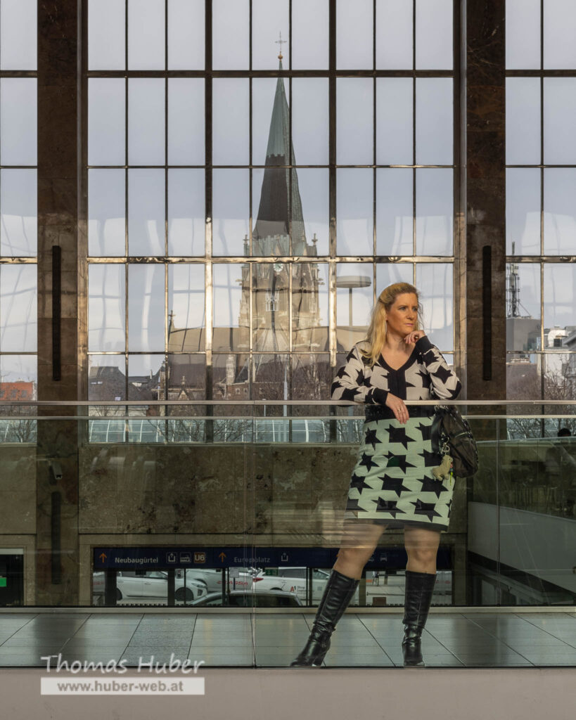 Lovely Crazy Woman steht bei Glasgeländer, großes Fenster mit Kirche im Hintergrund