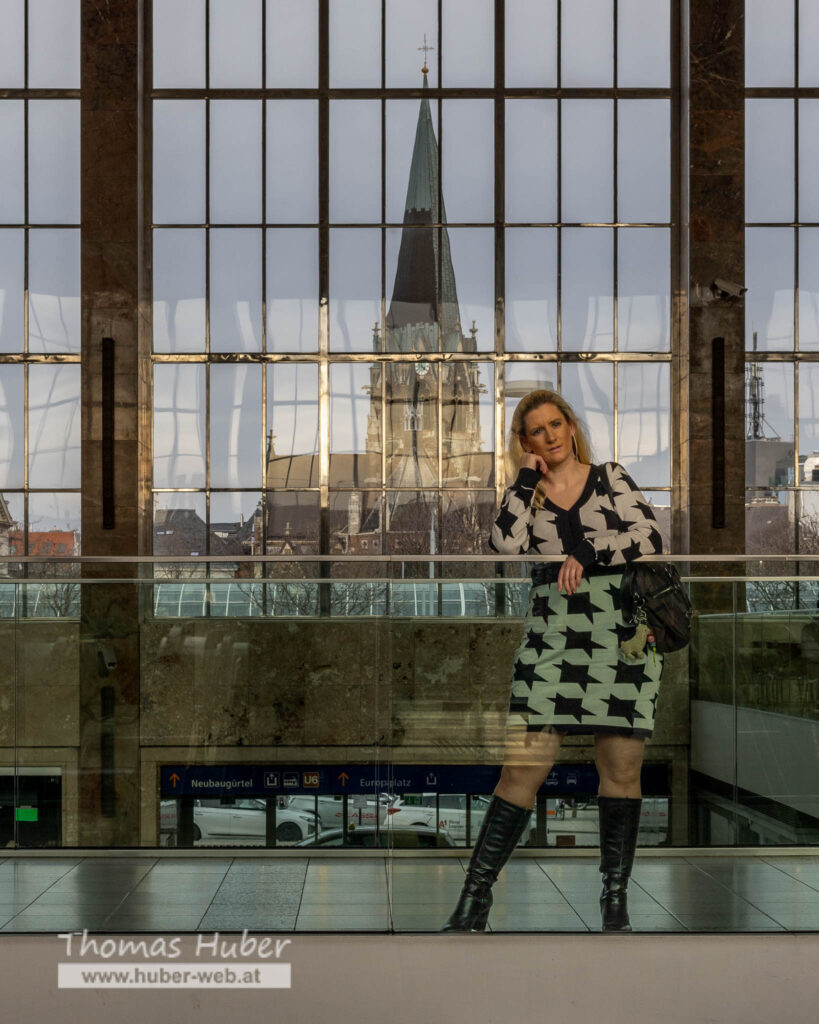 Lovely Crazy Woman steht bei Glasgeländer, großes Fenster mit Kirche im Hintergrund