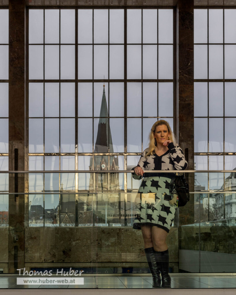 Lovely Crazy Woman steht bei Glasgeländer, großes Fenster mit Kirche im Hintergrund