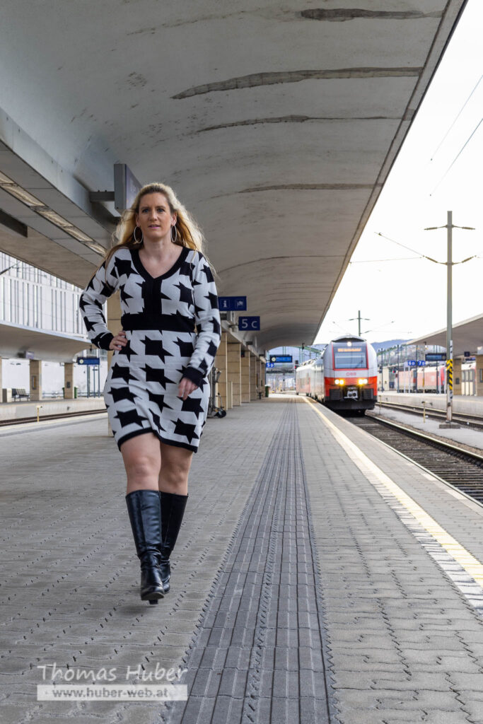 Lovely Crazy Woman geht am Bahnsteig, daneben fährt ein Zug ein