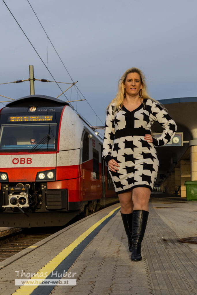 Lovely Crazy Woman geht am Bahnsteig, daneben fährt ein Zug ein